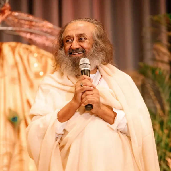 Gurudev Sri Sri Ravi Shankar smiling while speaking into a microphone