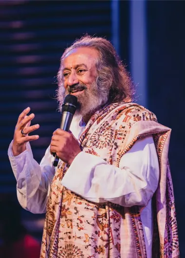 Gurudev Sri Sri Ravi Shankar speaking on stage with a microphone